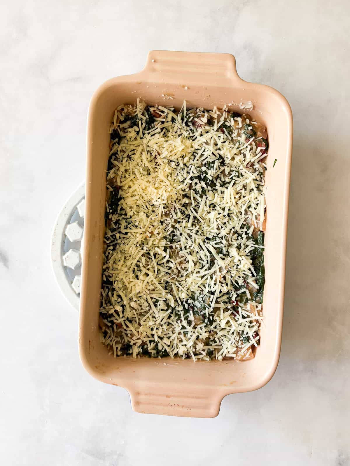This easy chard gratin is a naturally gluten-free, vegetarian side dish made with fresh chard, onion, cheese, and milk. Perfect for fall and winter. Place chard in a baking dish and cover with cheese.