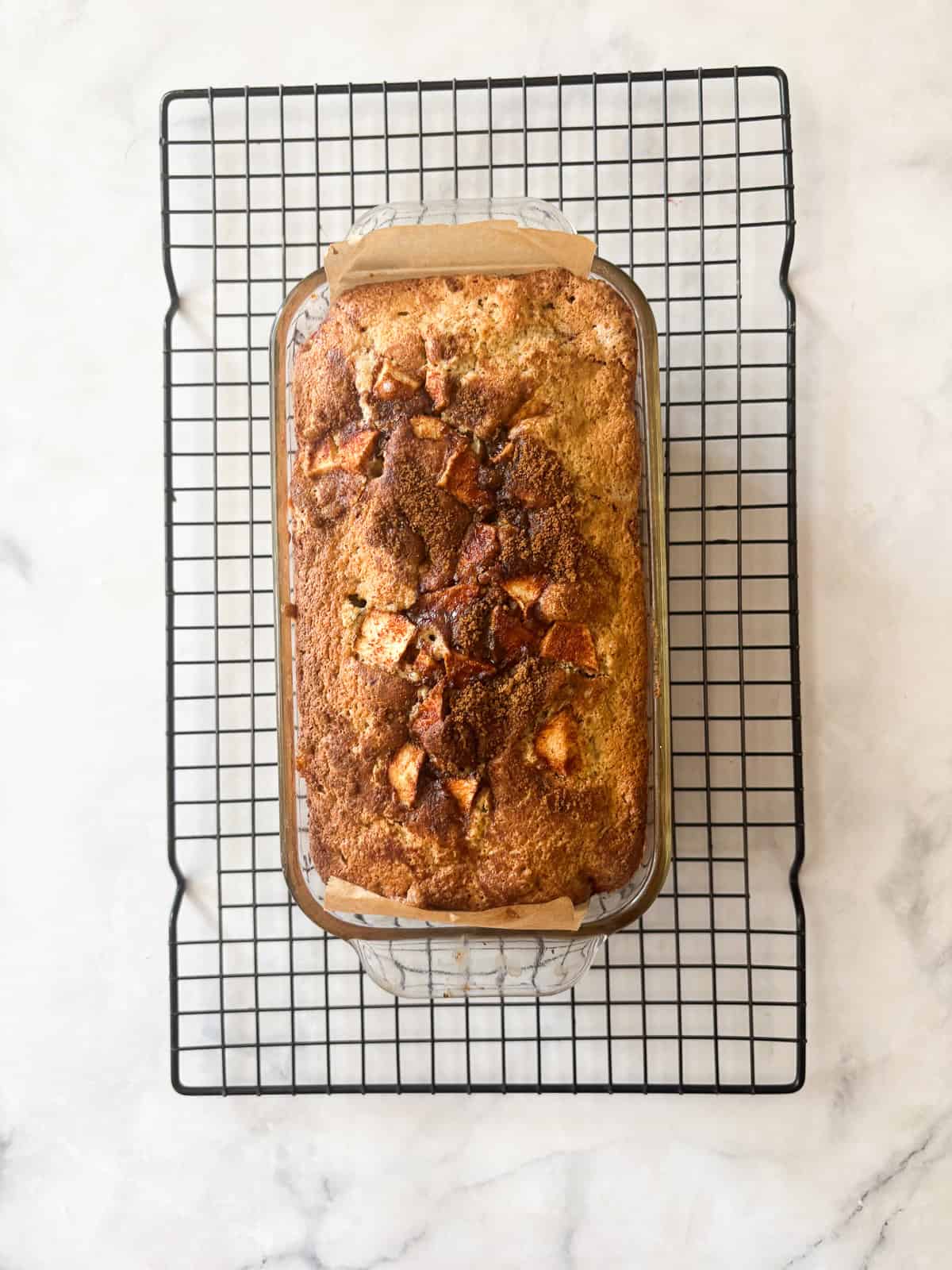 This gluten free apple bread is soft, buttery, and generously layered with fresh apples, cinnamon, and brown sugar. A one-bowl recipe! A loaf of gluten free apple bread cools on a rack.