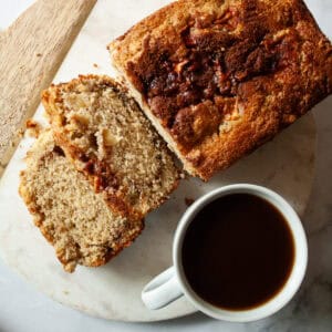 Slices cut from a gluten free apple bread loaf next to a cup of coffee.