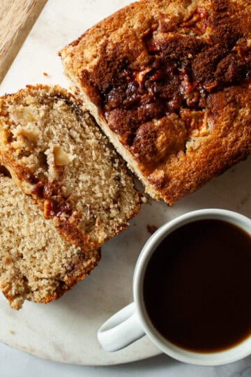 Slices cut from a gluten free apple bread loaf next to a cup of coffee.
