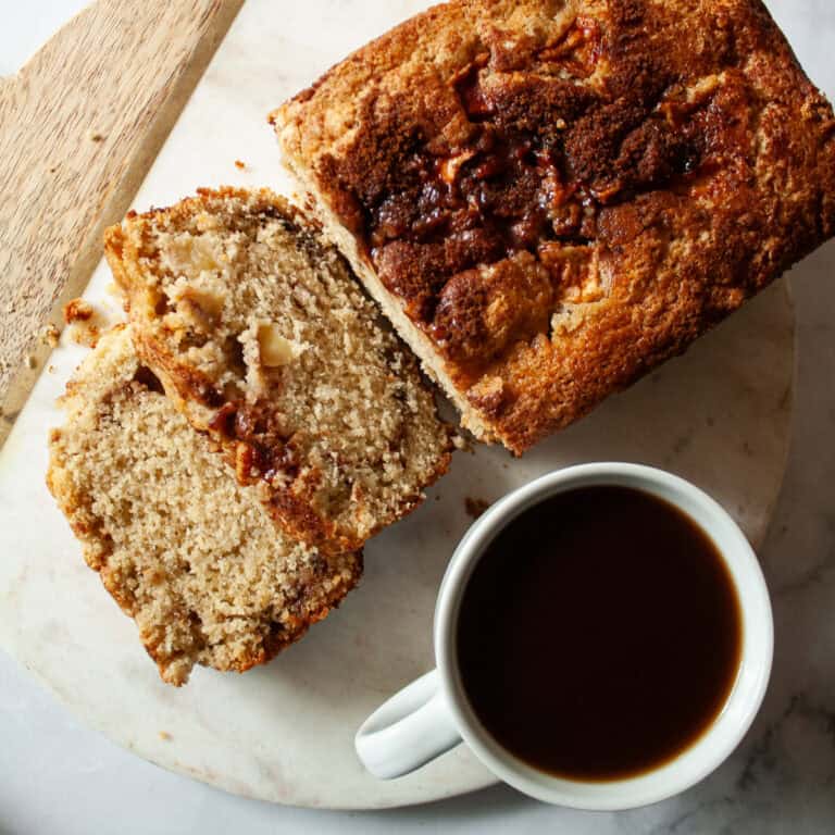 Slices cut from a gluten free apple bread loaf next to a cup of coffee.