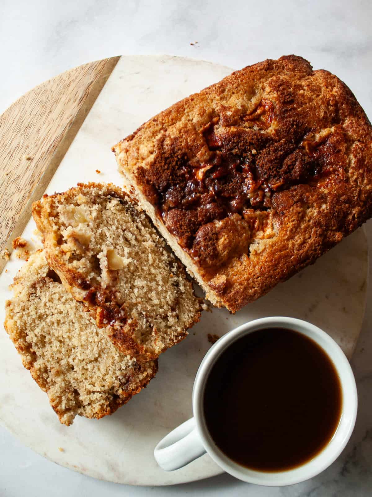 This gluten free apple bread is soft, buttery, and generously layered with fresh apples, cinnamon, and brown sugar. A one-bowl recipe! Slices cut from a gluten free apple bread loaf next to a cup of coffee.