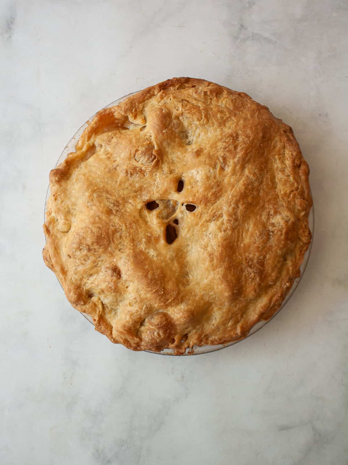 Make the most of the season's ripe apples with this gluten free apple pie that features tender slices of apples in a flaky gluten free crust. A gluten free apple pie on a marble counter.