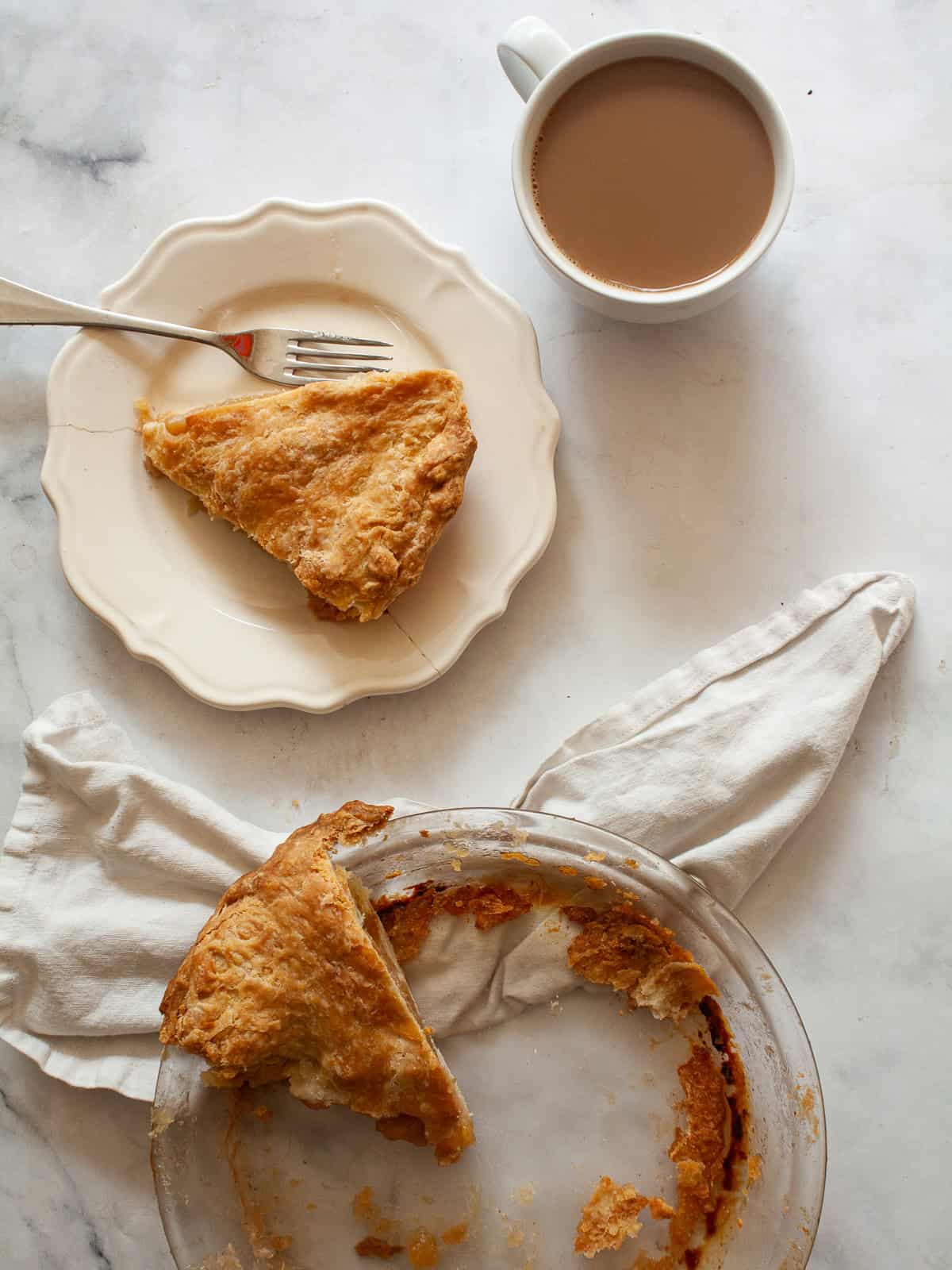 A cup of coffee next to a slice of gluten free Gravenstein apple pie and the pie plate.