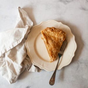 A slice of gluten free Gravenstein apple pie on a plate with a fork and a napkin.