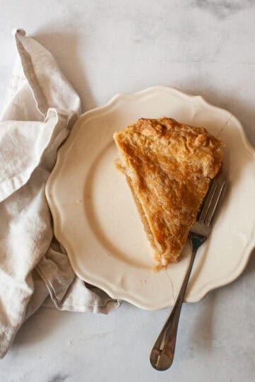 A slice of gluten free Gravenstein apple pie on a plate with a fork and a napkin.