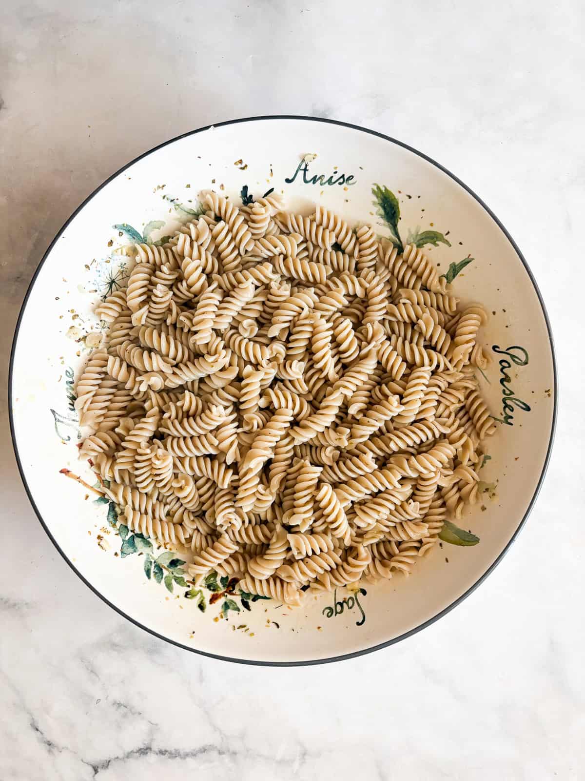 A summer staple, my gluten free pasta salad recipe features a zingy lemon dressing, fresh mozzarella, tomatoes, and fresh herbs. Gluten free pasta is added to dressing in a bowl for gluten free pasta salad.
