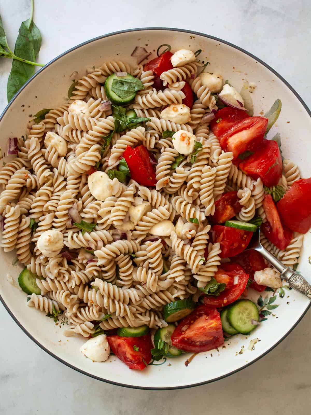 Tomatoes, cucumber, basil and mozzarella in a bowl of gluten free pasta salad.