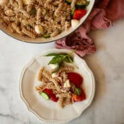 A serving of gluten free pasta salad on a plate and the bowl of salad is seen behind it.