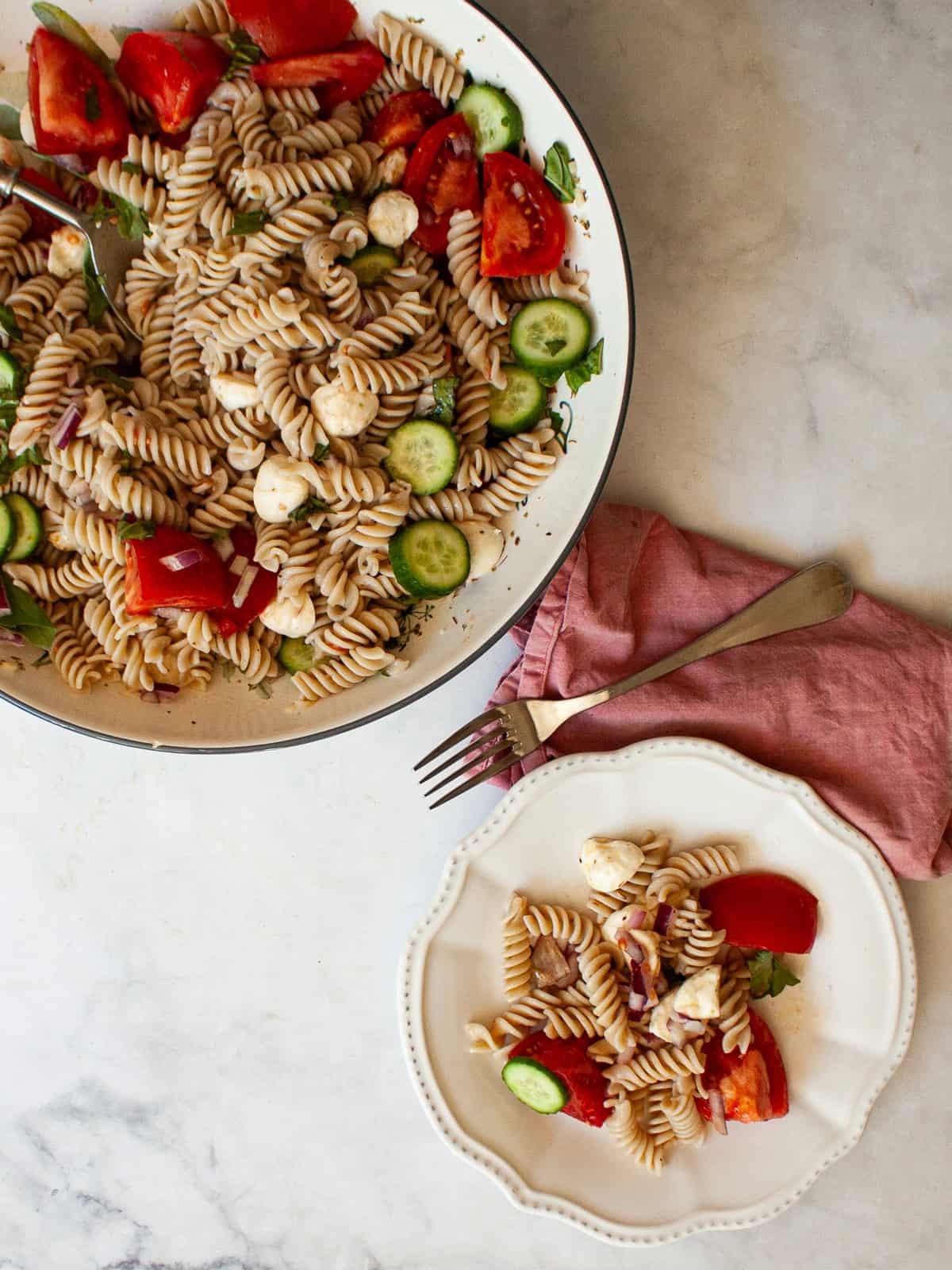 A summer staple, my gluten free pasta salad recipe features a zingy lemon dressing, fresh mozzarella, tomatoes, and fresh herbs. A serving of gluten free pasta salad on a plate and the bowl of salad.