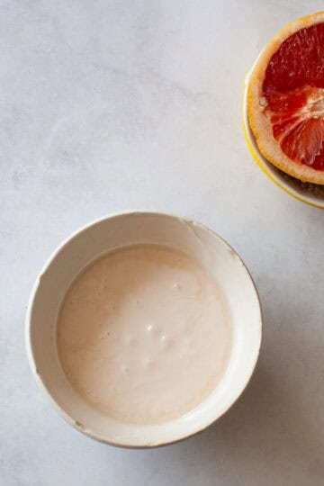 Grapefruit glaze in a bowl with a half of a grapefruit next to it.