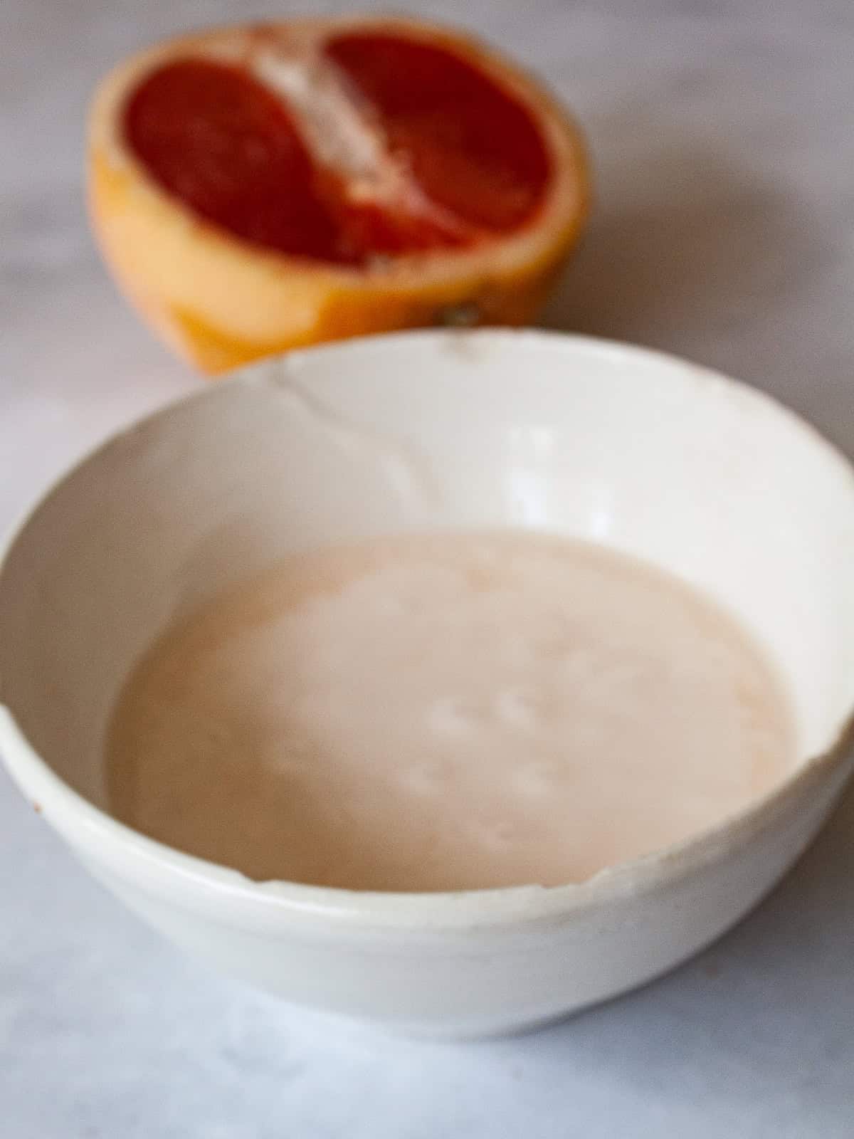 A sweet, lightly pink grapefruit glaze that is so lovely on loaf cakes, regular cakes, cookies, and anywhere else you need a flavor boost! A bowl of grapefruit glaze and a grapefruit behind it.