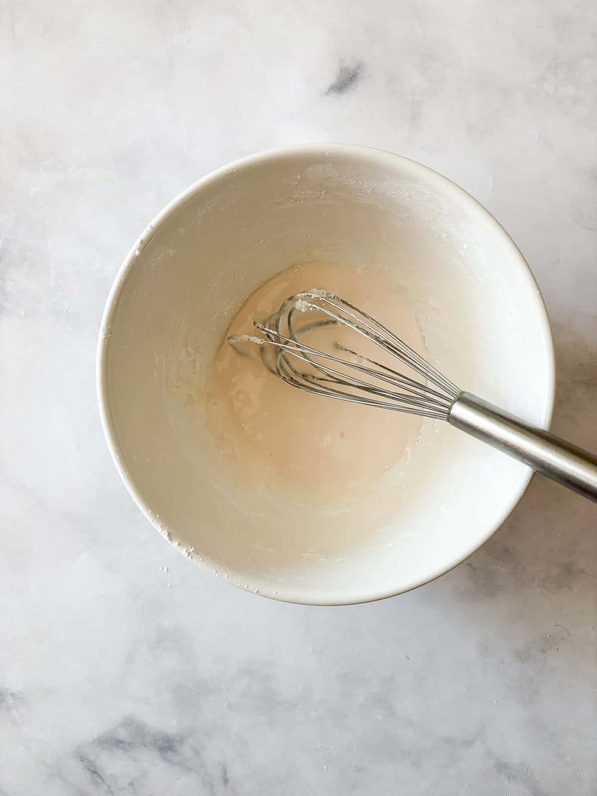 A sweet, lightly pink grapefruit glaze that is so lovely on loaf cakes, regular cakes, cookies, and anywhere else you need a flavor boost! A whisk combines grapefruit glaze in a bowl.