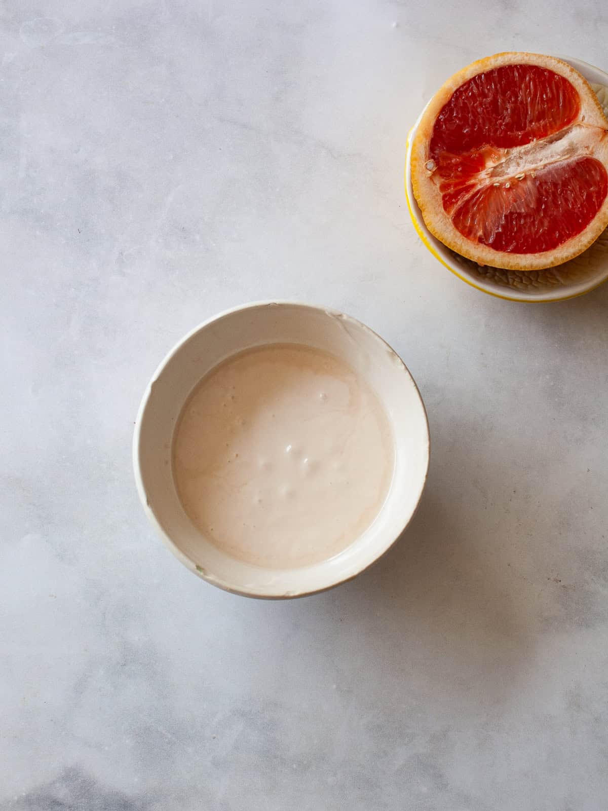 Grapefruit glaze in a bowl with a half of a grapefruit next to it.