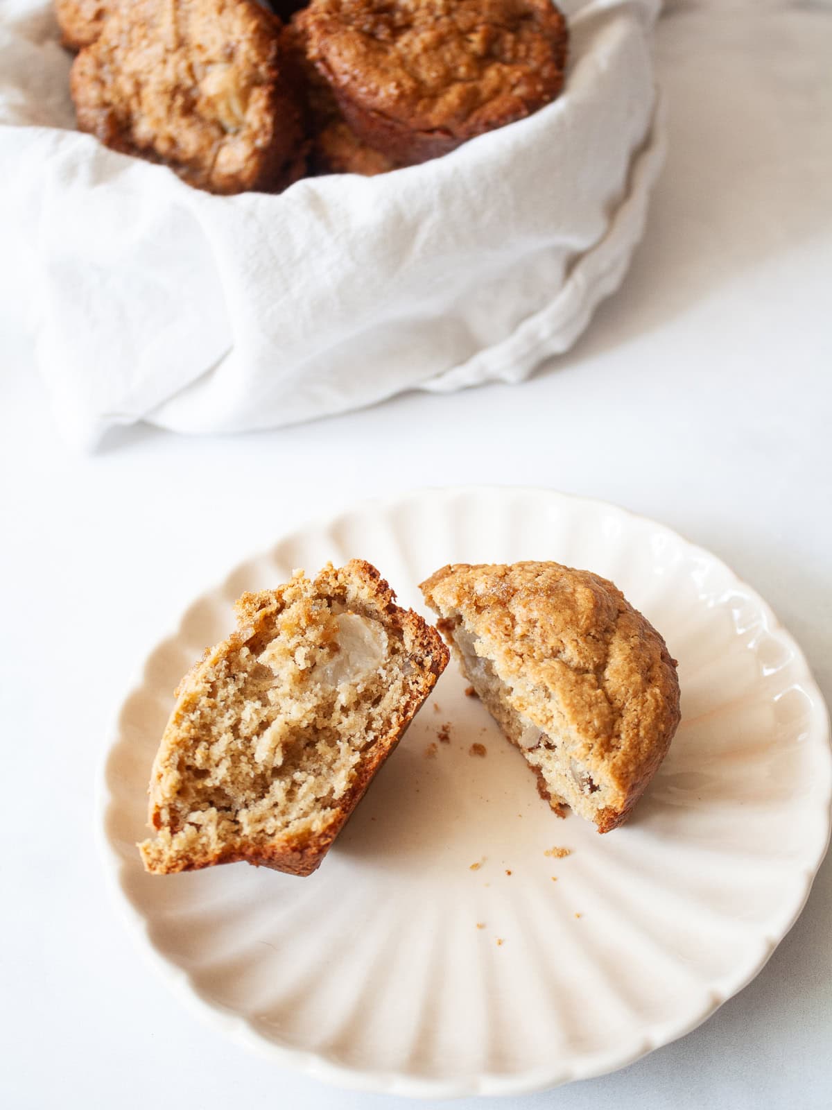 Loaded with fresh, juicy pears, these whole grain pear muffins are studded with walnuts and finished with a crunchy cap of brown sugar. A pear muffin cut in half on a plate.