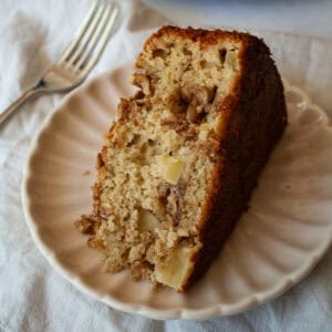 A slice of apple crumb cake on a plate with a fork next to it.
