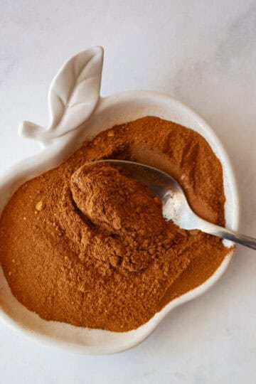 A spoon dips into a bowl in an apple shape that holds apple pie spice.