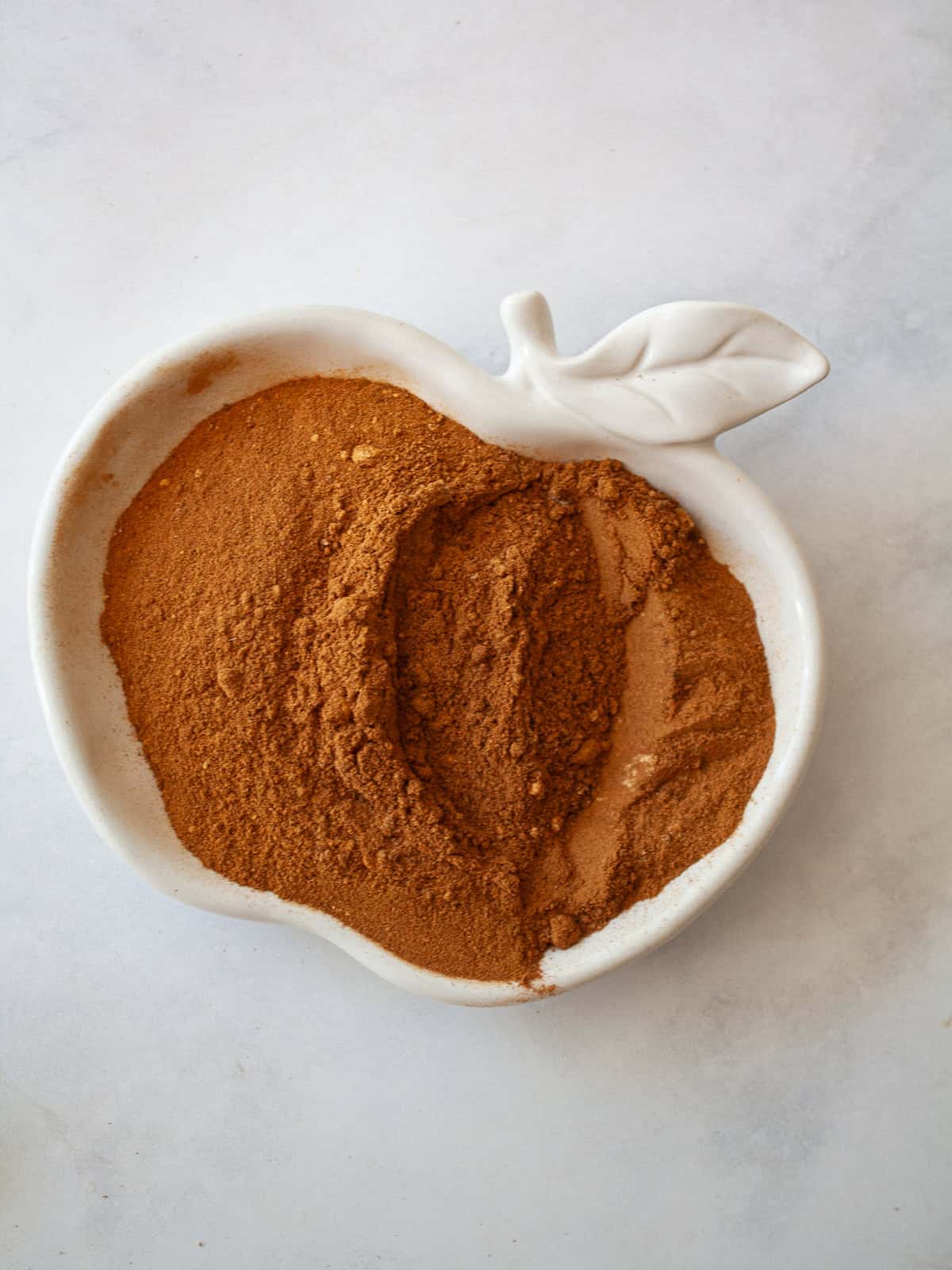 Make easy homemade apple pie spice with cinnamon, nutmeg, ginger, allspice, cloves, and cardamom. Perfect for fall baking! An apple shaped dish full of apple pie spice.