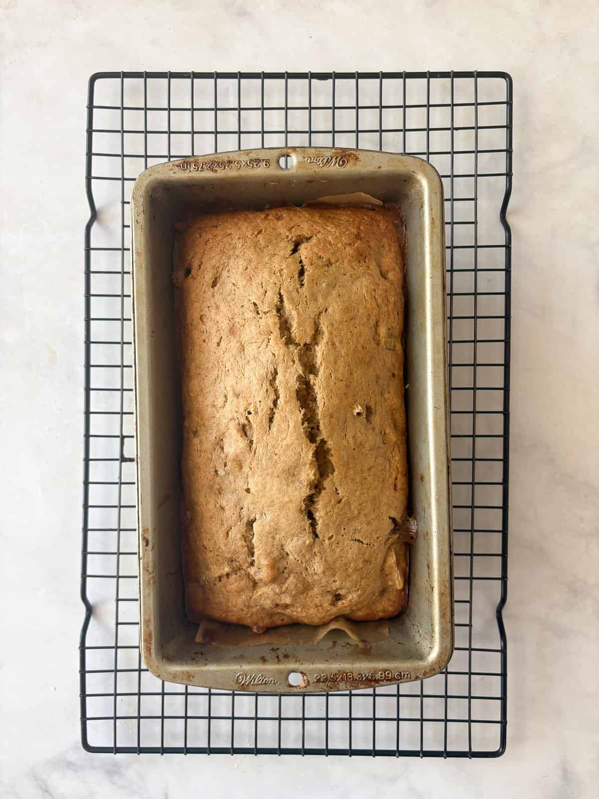 Easy banana pear bread made with whole wheat or gluten-free oat flour, juicy pears, and walnuts. A tender quick bread for fall and beyond. A baked loaf of banana pear bread cools in a pan.