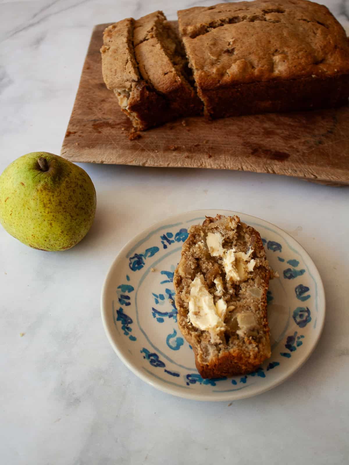 Easy banana pear bread made with whole wheat or gluten-free oat flour, juicy pears, and walnuts. A tender quick bread for fall and beyond. A slice of banana pear with butter on a plate, a loaf on a cutting board, and a pear.