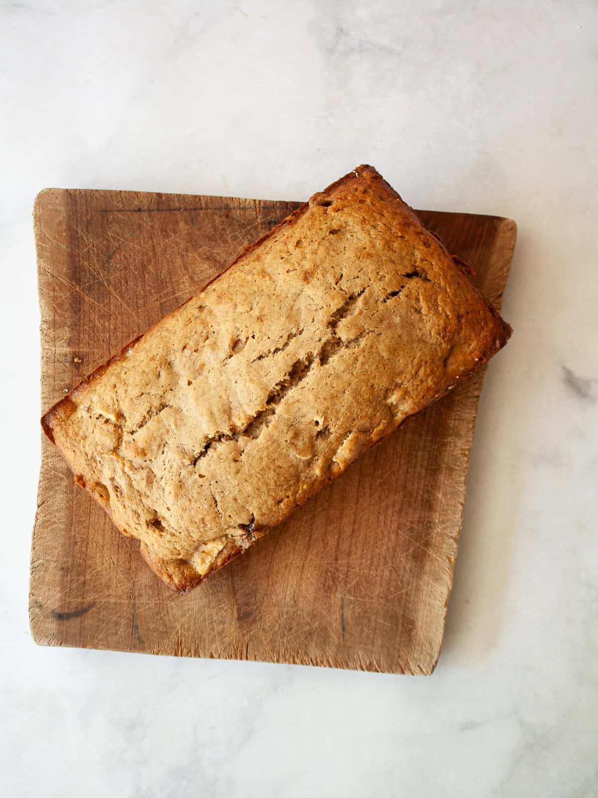 Easy banana pear bread made with whole wheat or gluten-free oat flour, juicy pears, and walnuts. A tender quick bread for fall and beyond. A loaf of banana pear bread on a wooden cutting board.
