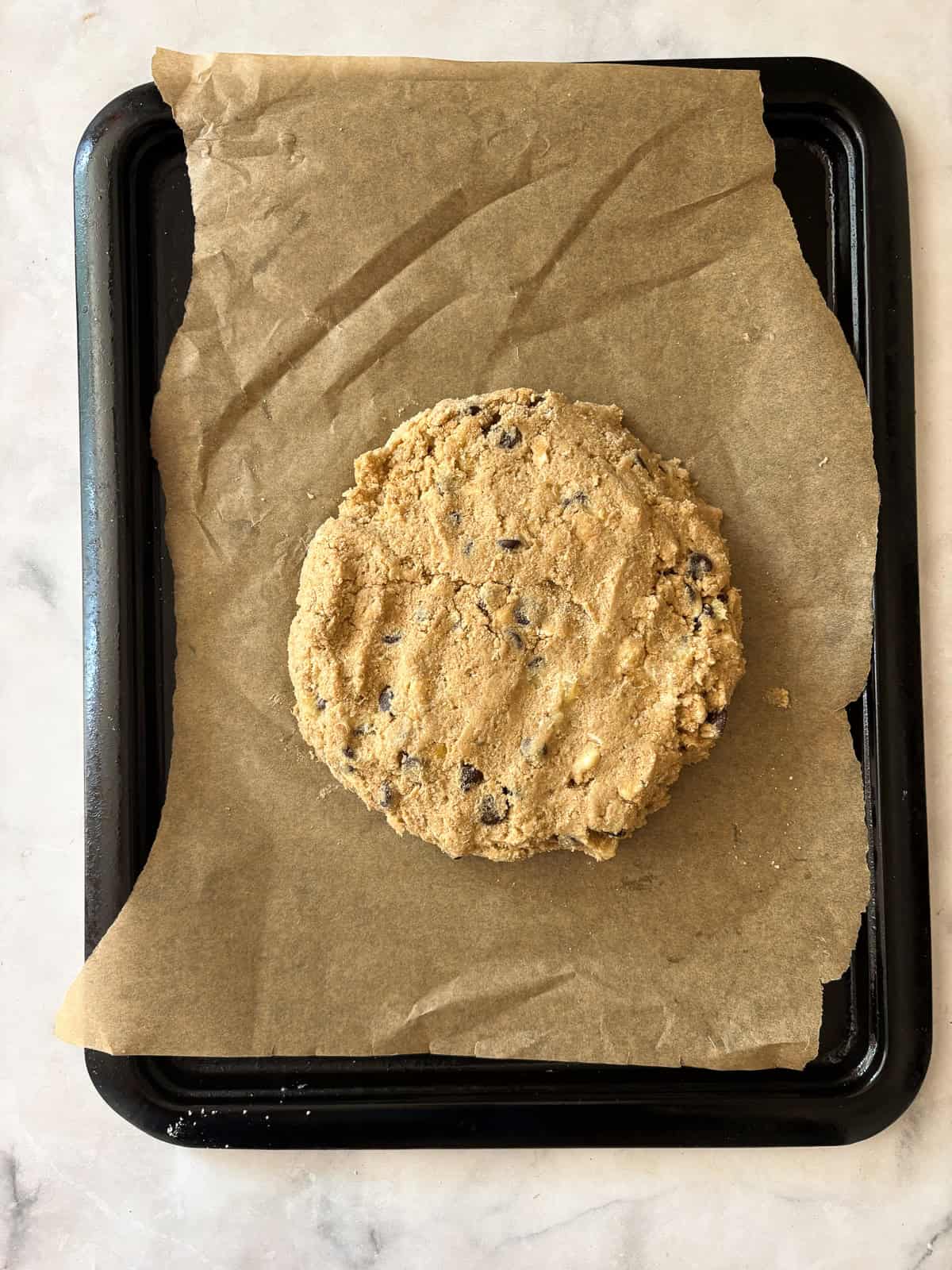 These whole grain banana scones are filled with chocolate chips, cinnamon, and a whole ripe banana for a tender, lightly sweet treat. A round of banana scones dough on a lined baking sheet.