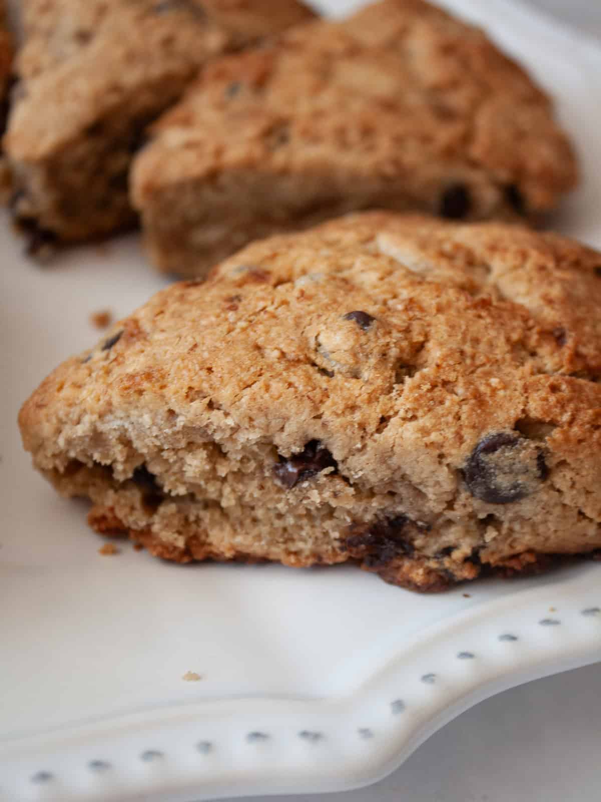 These whole grain banana scones are filled with chocolate chips, cinnamon, and a whole ripe banana for a tender, lightly sweet treat. A side view of a banana scone with chocolate chips on a plate.