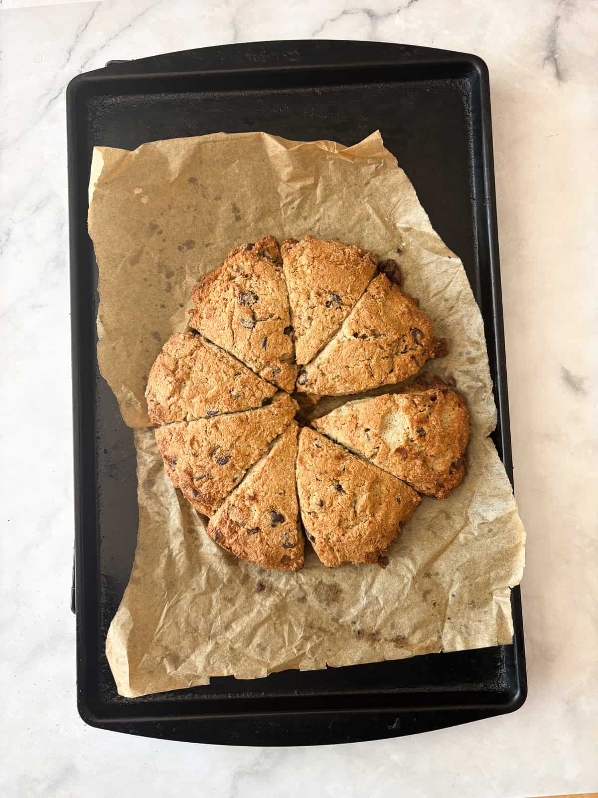 These whole grain banana scones are filled with chocolate chips, cinnamon, and a whole ripe banana for a tender, lightly sweet treat. Baked banana scones cool on a baking sheet.