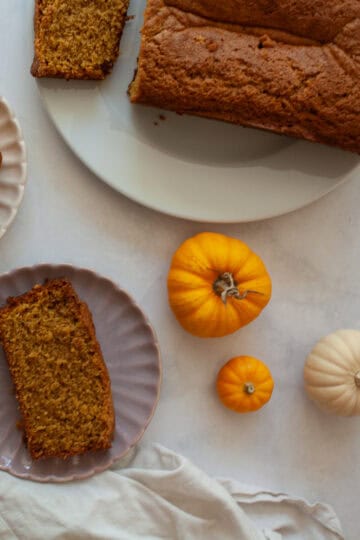 Slices of gluten free pumpkin bread, mini pumpkins, and the loaf of bread.