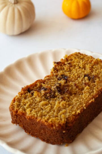 A slice of gluten free pumpkin chocolate chip bread on a plate with mini pumpkins next to it.