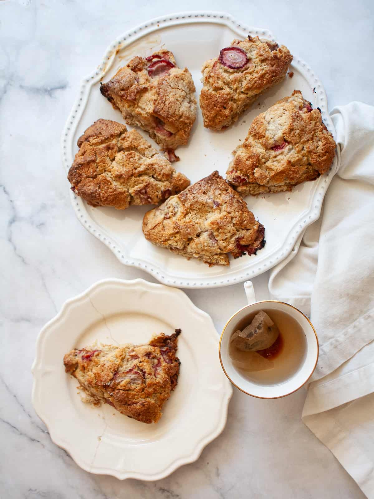 The simplest, tenderest gluten free oat flour scones that are made just with oat flour. Use this recipe as your base for all sorts of add-ins, from fruit, to chocolate, to maple syrup. A plate of oat flour scones, a cup of tea, and one on a plate.