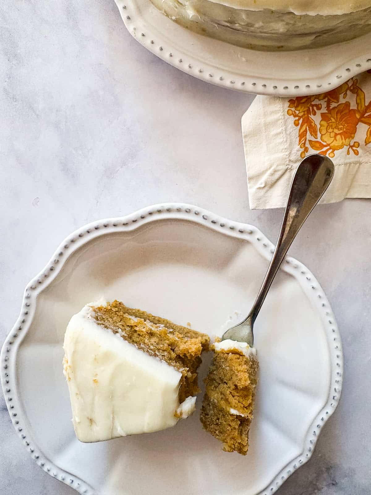 This beautiful gluten free pumpkin layer cake is rich and moist, warmly spiced, and frosted with a plush, sweet-tangy cream cheese frosting. A fork cuts into a piece of gluten free pumpkin layer cake on a plate.