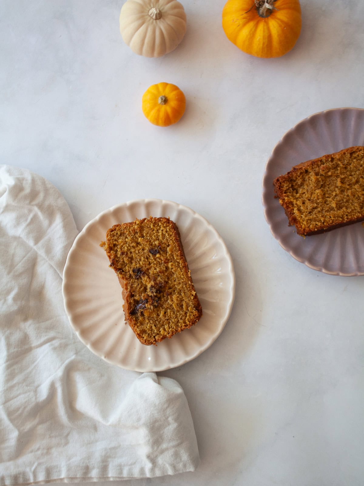This gluten-free olive oil pumpkin bread is rich, moist, and full of fall spices. Made with oat and almond flours, it's easy to customize! Two slices of gluten free olive oil pumpkin bread on plates with some mini pumpkins next to them.