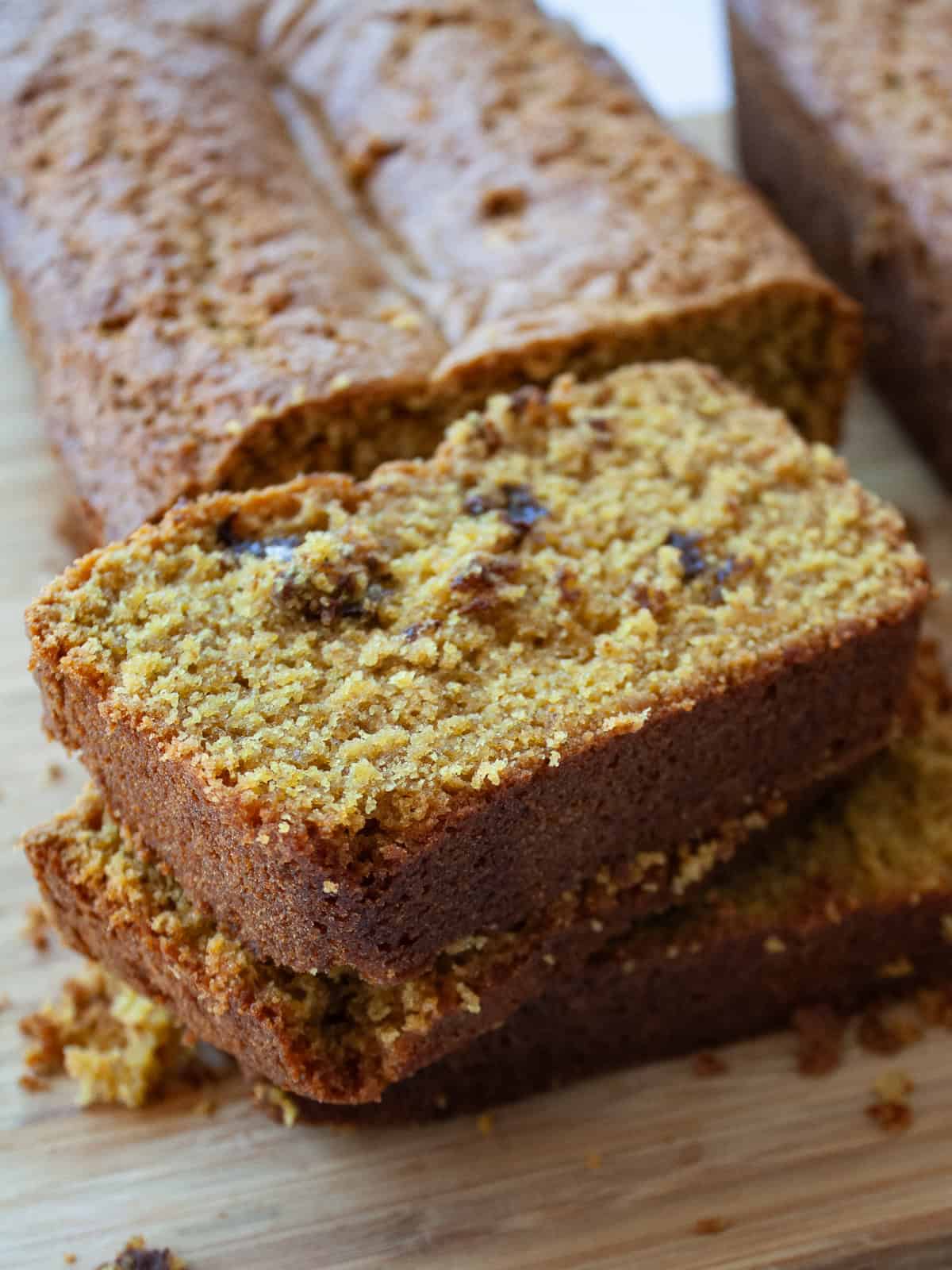 This gluten-free olive oil pumpkin bread is rich, moist, and full of fall spices. Made with oat and almond flours, it's easy to customize! Stacked slices of olive oil pumpkin bread on a wooden cutting board.