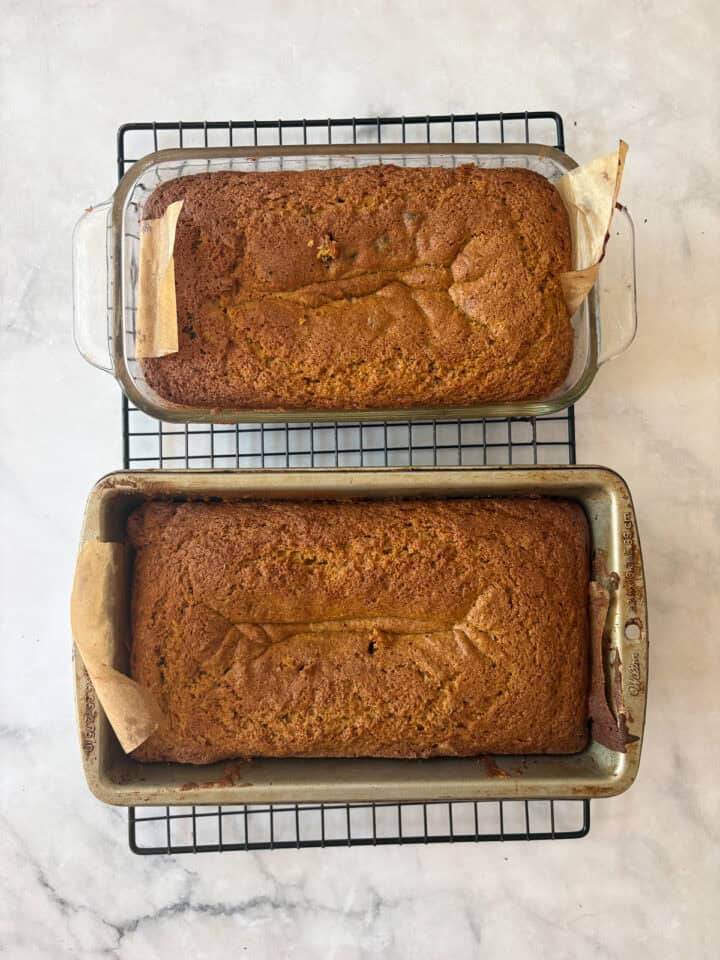 This gluten-free olive oil pumpkin bread is rich, moist, and full of fall spices. Made with oat and almond flours, it's easy to customize! Two baked loaves of gluten free olive oil pumpkin bread cool in pans on a rack.