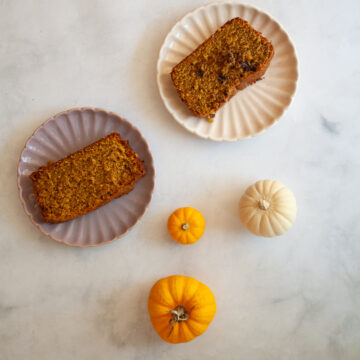 Two slices of gluten free olive oil pumpkin bread on plates with some mini pumpkins next to them.