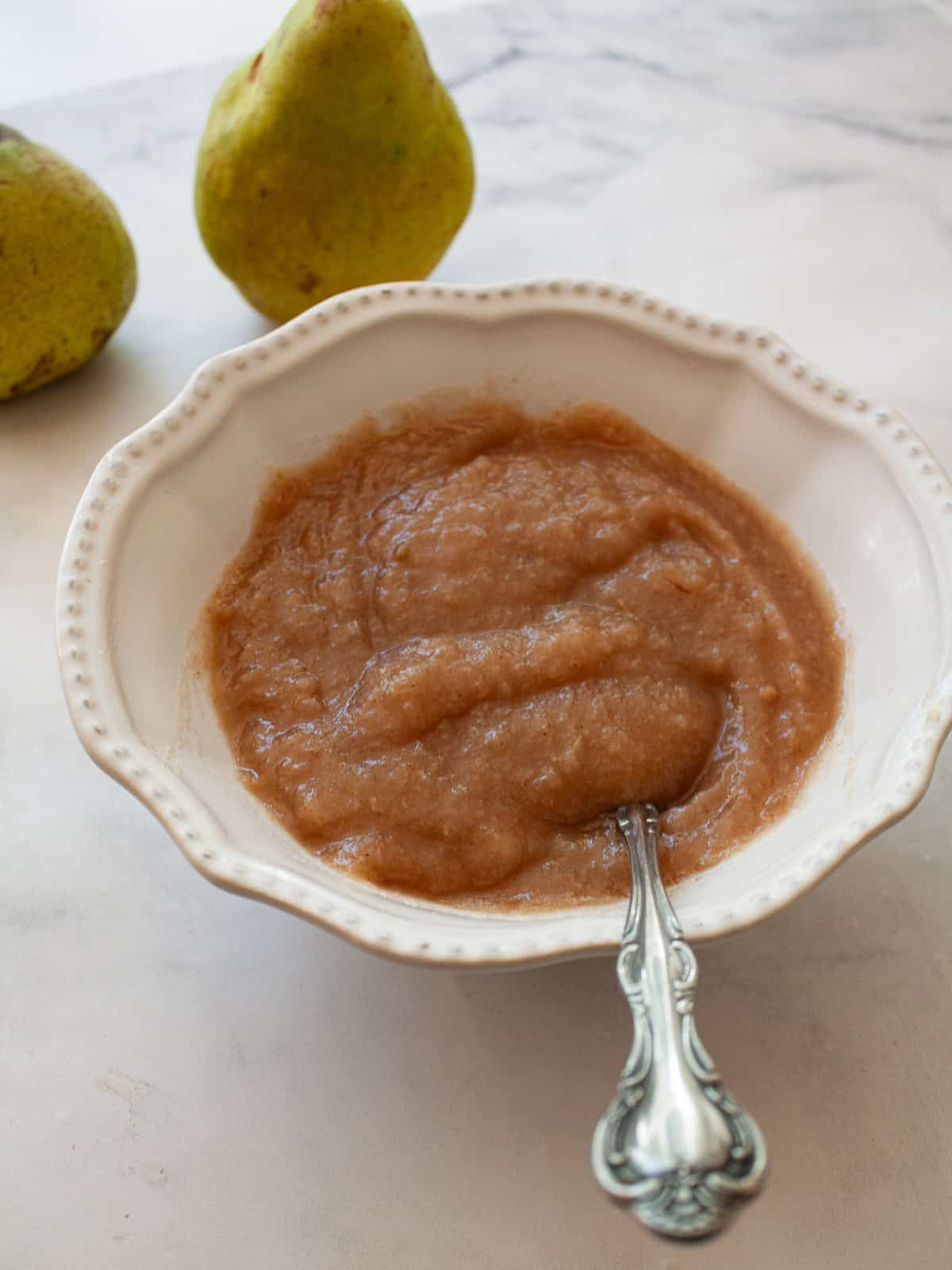 A smooth, sweet pear sauce that's best made with ripe pears! Add cinnamon and maple syrup if you like, or enjoy it plain. A bowl of pear sauce with a spoon and pears.