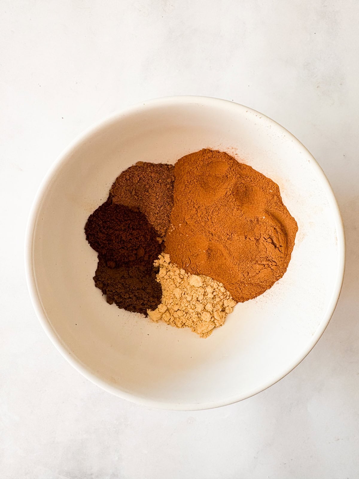 A homemade, versatile pumpkin spice blend with cinnamon, nutmeg, ginger, cloves, and allspice. Great in pies, muffins, quick breads, and more! Spices are placed in a bowl to make pumpkin spice blend.