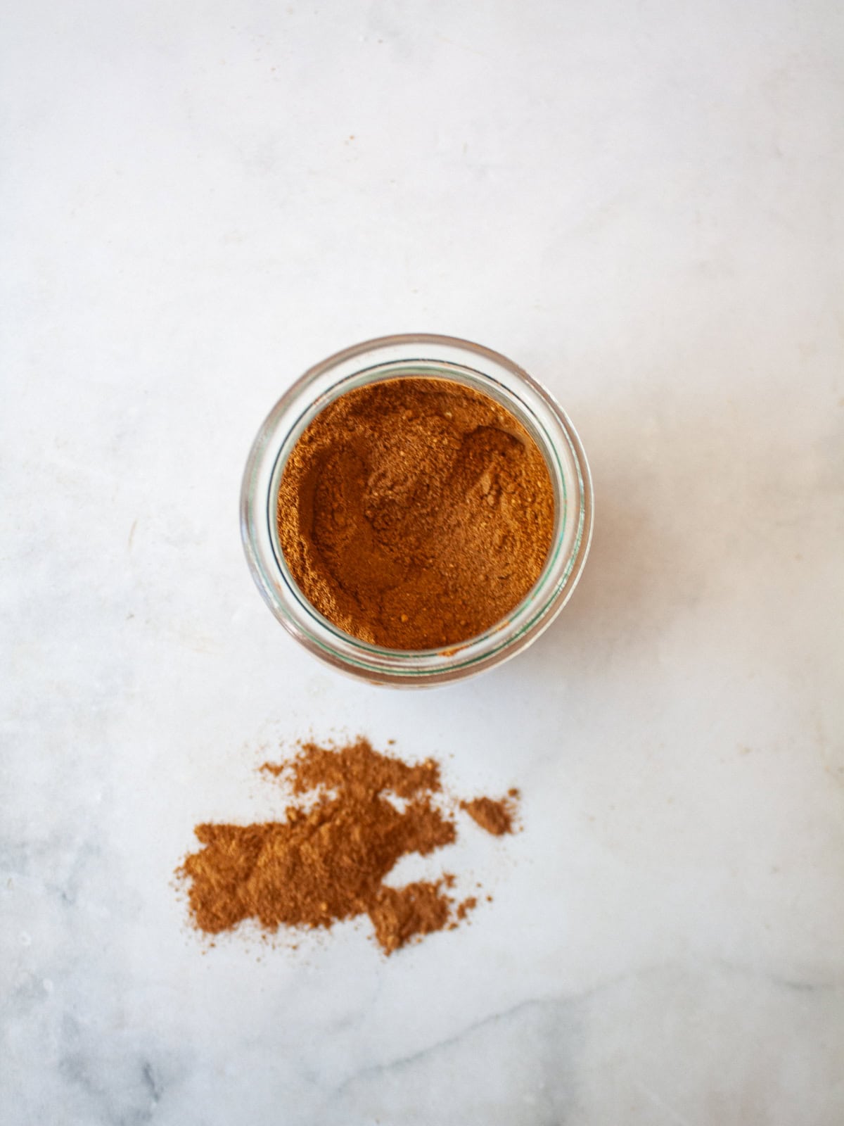 A homemade, versatile pumpkin spice blend with cinnamon, nutmeg, ginger, cloves, and allspice. Great in pies, muffins, quick breads, and more! Homemade pumpkin spice blend in a jar and a little in front of it.