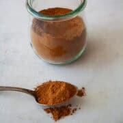 A spoon with homemade pumpkin spice blend in front of a jar of spice blend.