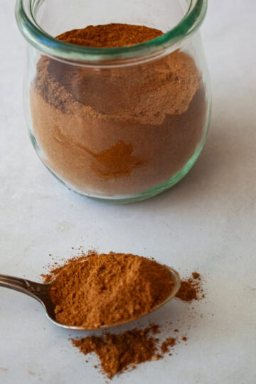 A spoon with homemade pumpkin spice blend in front of a jar of spice blend.