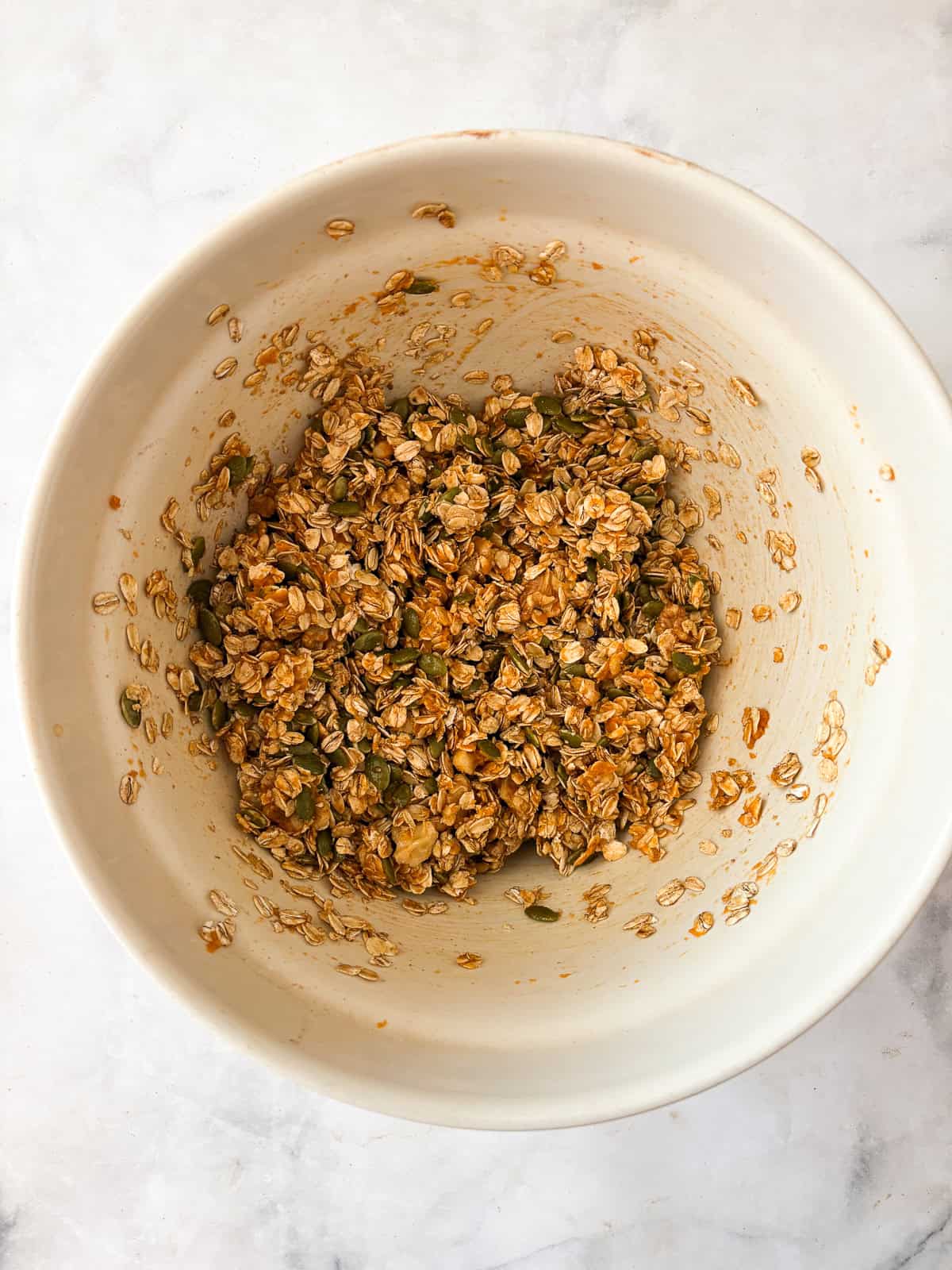 Enjoy this pumpkin spice granola that's made with pumpkin puree, warm spices, crunchy walnuts and pumpkin seeds, olive oil, and maple syrup. Mixing in maple syrup, pumpkin, and olive oil to pumpkin spice granola.