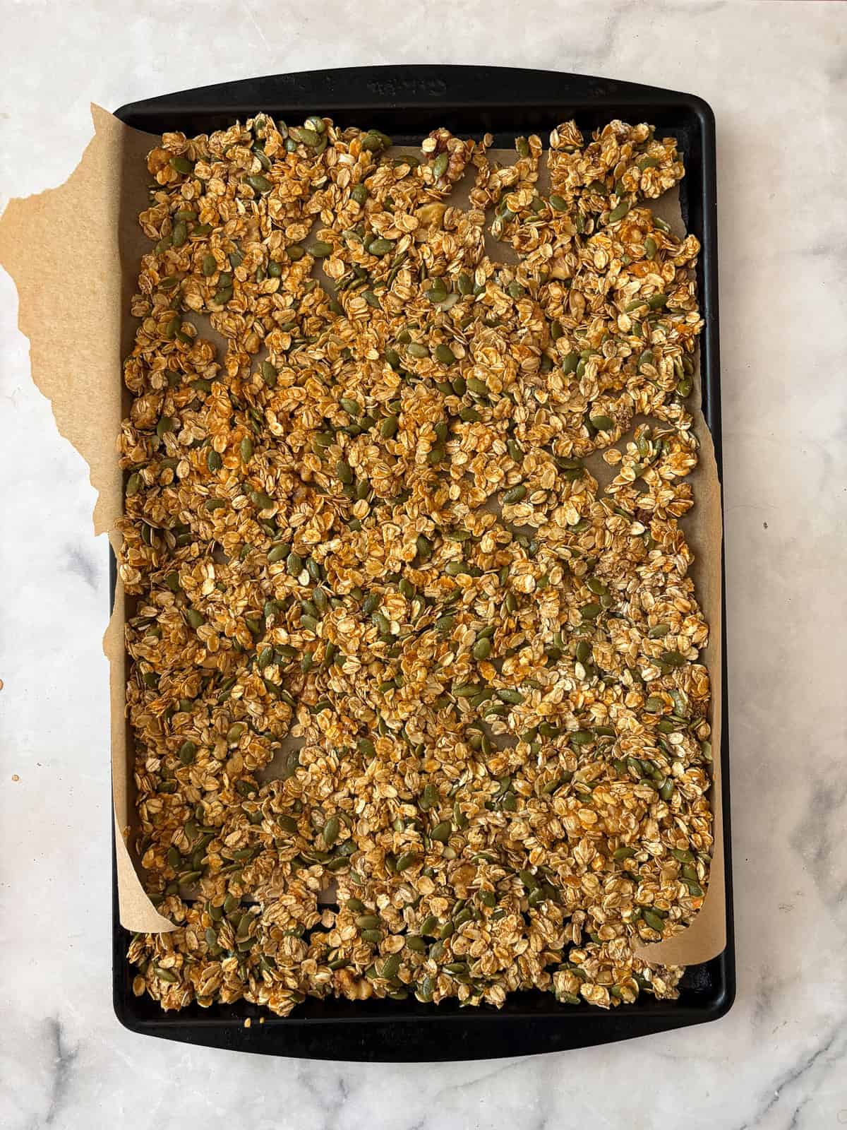 Enjoy this pumpkin spice granola that's made with pumpkin puree, warm spices, crunchy walnuts and pumpkin seeds, olive oil, and maple syrup. A tray of pumpkin spice granola before the ven.