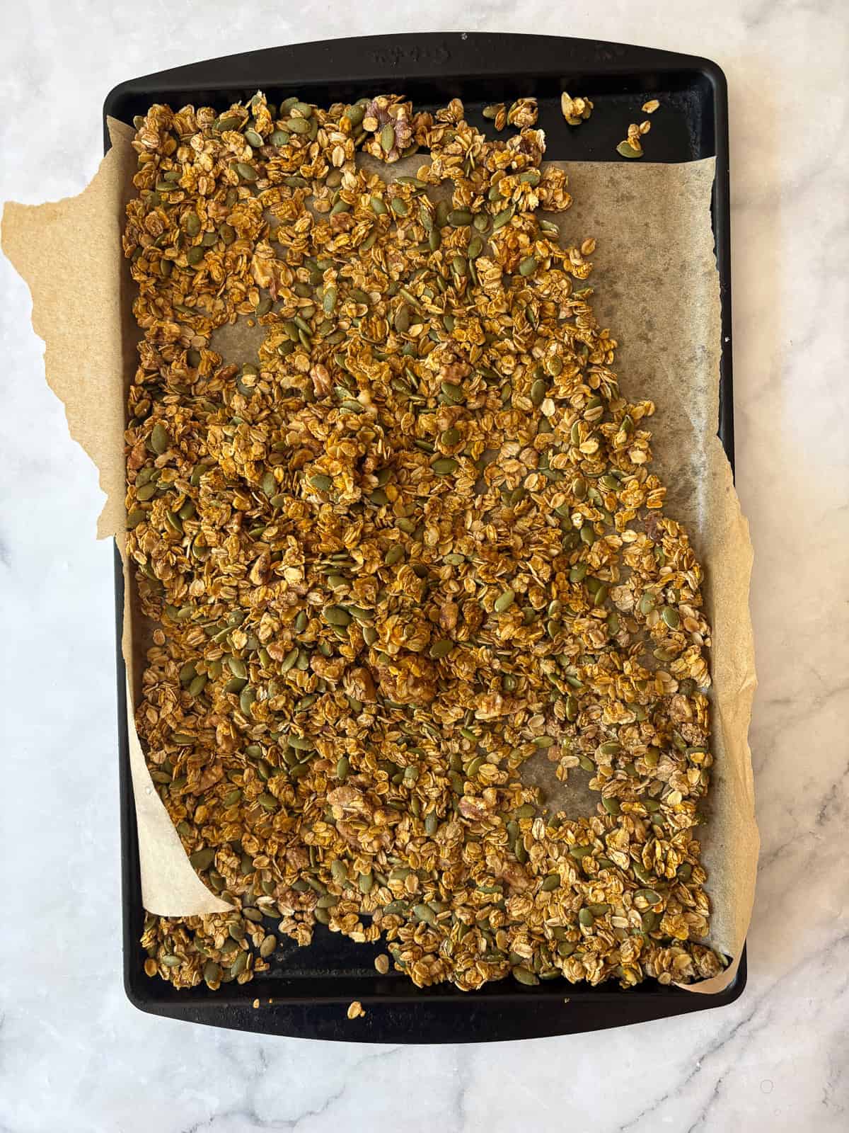 Enjoy this pumpkin spice granola that's made with pumpkin puree, warm spices, crunchy walnuts and pumpkin seeds, olive oil, and maple syrup. A baking sheet of pumpkin spice granola cools.