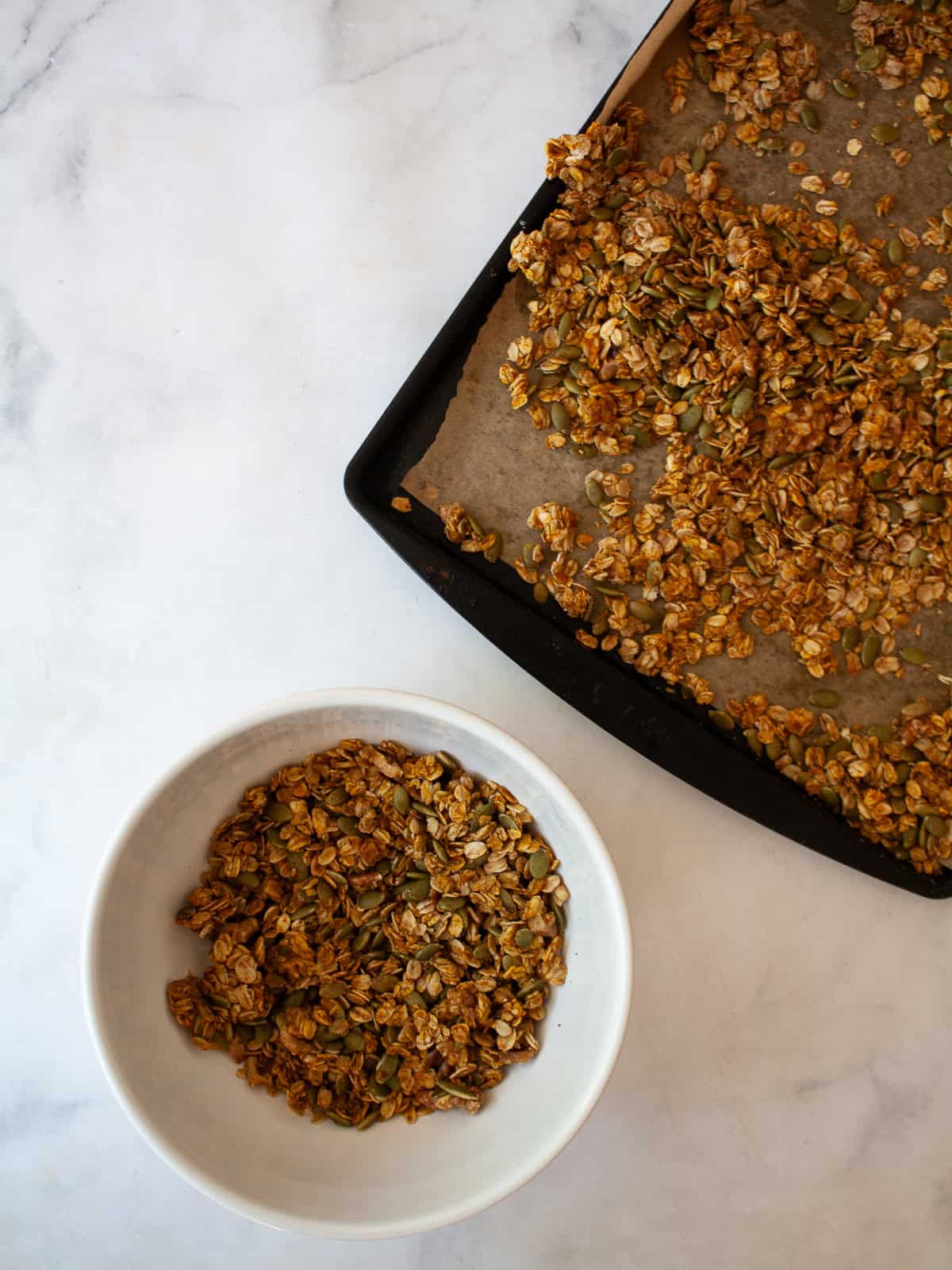 A bowl of pumpkin spice granola and a tray of granola.