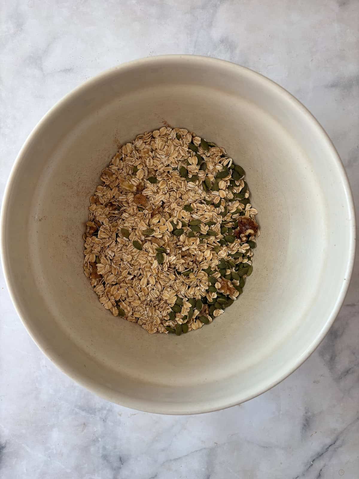 Enjoy this pumpkin spice granola that's made with pumpkin puree, warm spices, crunchy walnuts and pumpkin seeds, olive oil, and maple syrup. Mixing dry ingredients in a bowl for pumpkin spice granola.