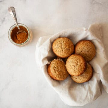 A bowl of spice muffins next to a jar of spice.