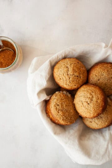 A bowl of spice muffins next to a jar of spice.